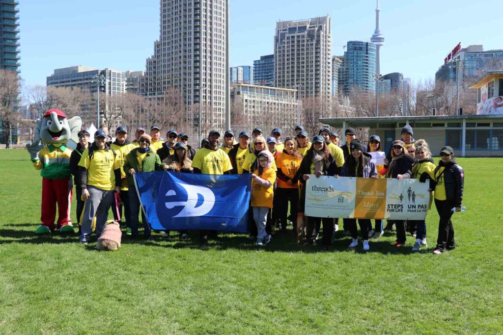 A group of 20-30 people gather in a park. They're holding banners and smiling in front of the Toronto skyline.