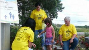 a young girl waters flowers while three adults in yellow t-shirts watch on