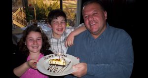 Man holds Happy Birthday cake with young girl and boy