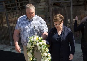 Man and woman carry yellow and white wreath