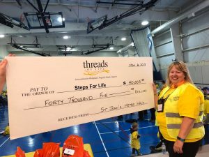 Smiling woman stands in front of presentation cheque made out to Steps for Life for $40,005.53