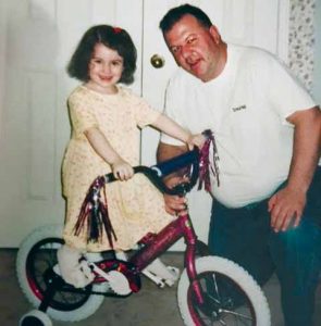 Young girl in yellow dress sits on bike with man proudly crouched beside