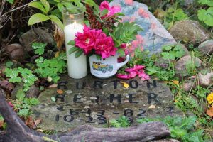 candle and flowers rest above headstone that reads Burton Reimer 6-13-82 - 10-23-99
