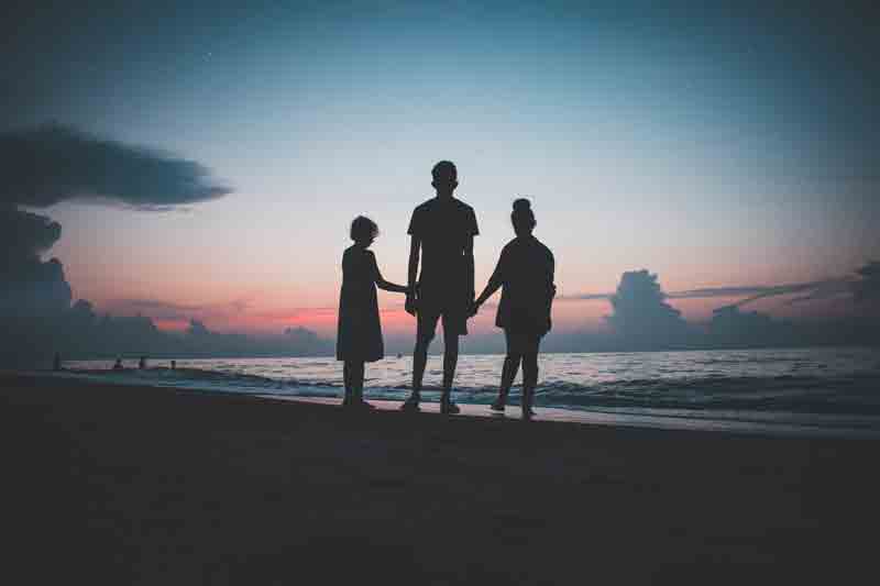 backlit silhouettes of three kids on a beach at sunset