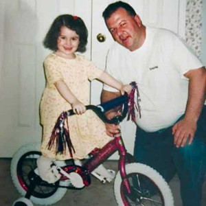 Young girl sitting on bike beside a man, crouched down beside her