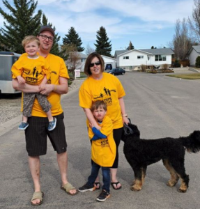 man and woman with two young children walking with their dog. All are wearing yellow T-shirts.