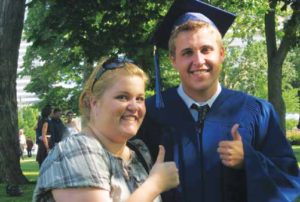 A young man in blue cap and gown making a thumbs up with a young woman