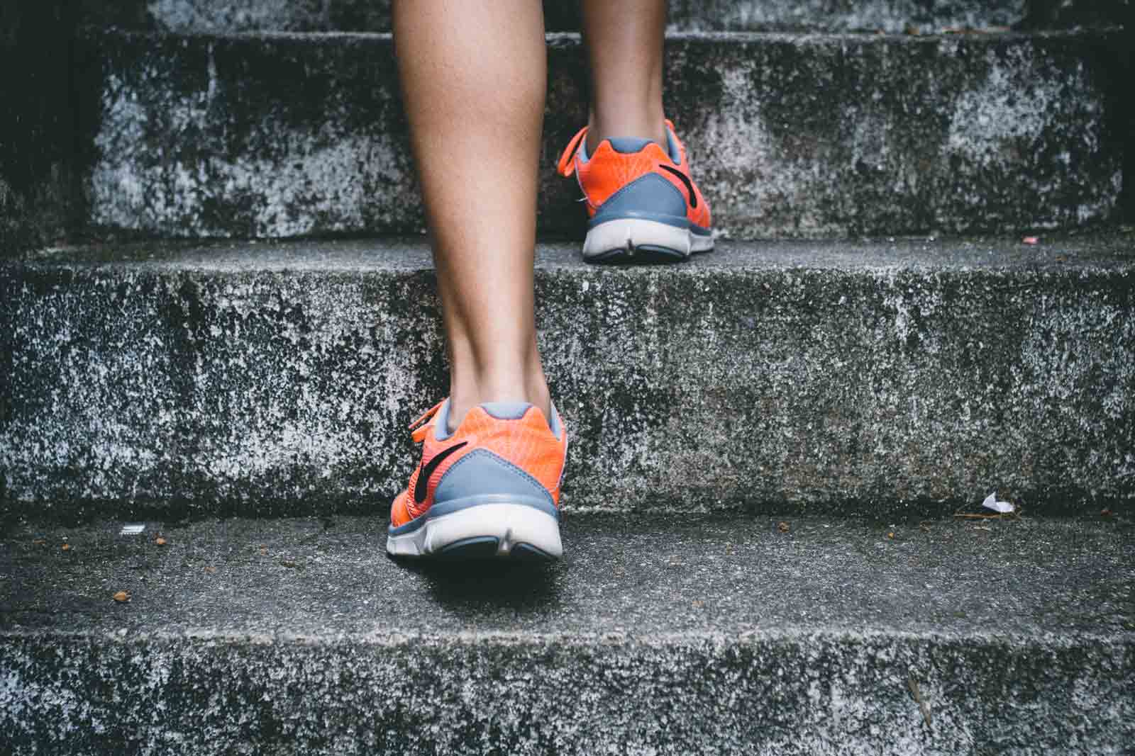 Close up of person climbing cement stairs. They are wearing grey and orange running shoes. 