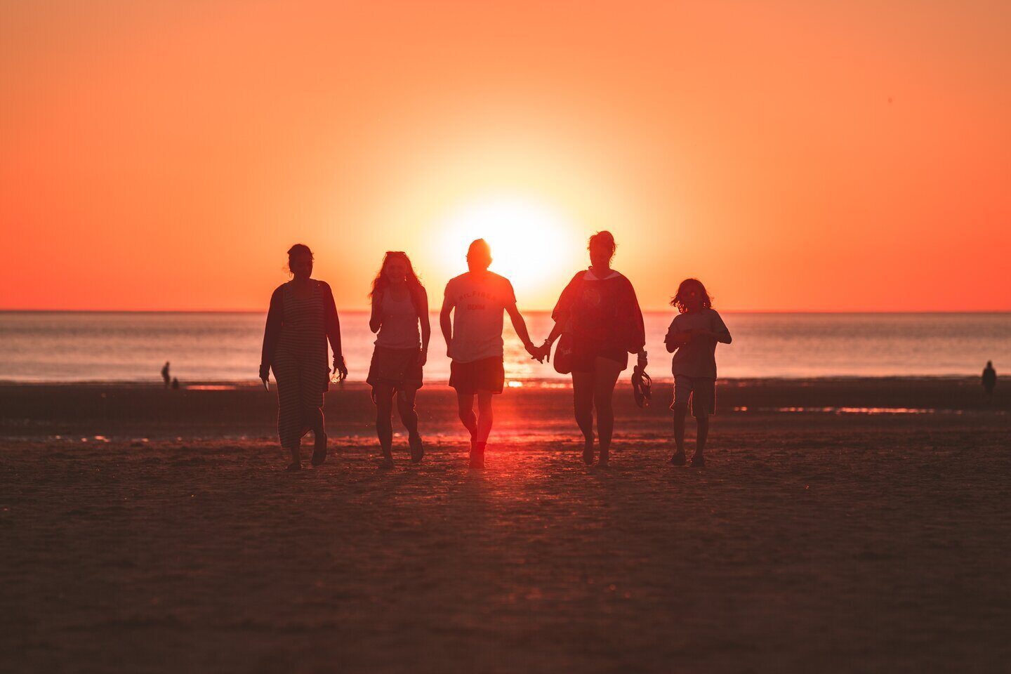 Silhouettes of five people facing a sunset over the water.