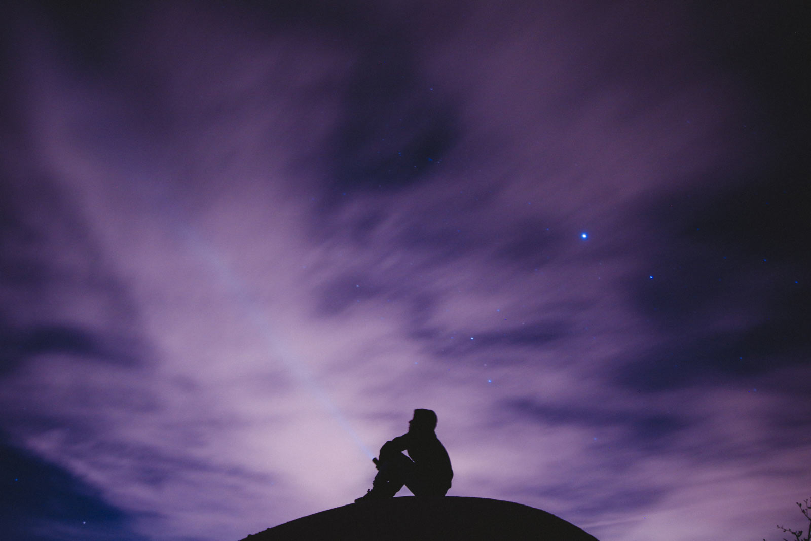 Silhouette of person in front of a cloudy night sky. One star in particular shines very brightly above.
