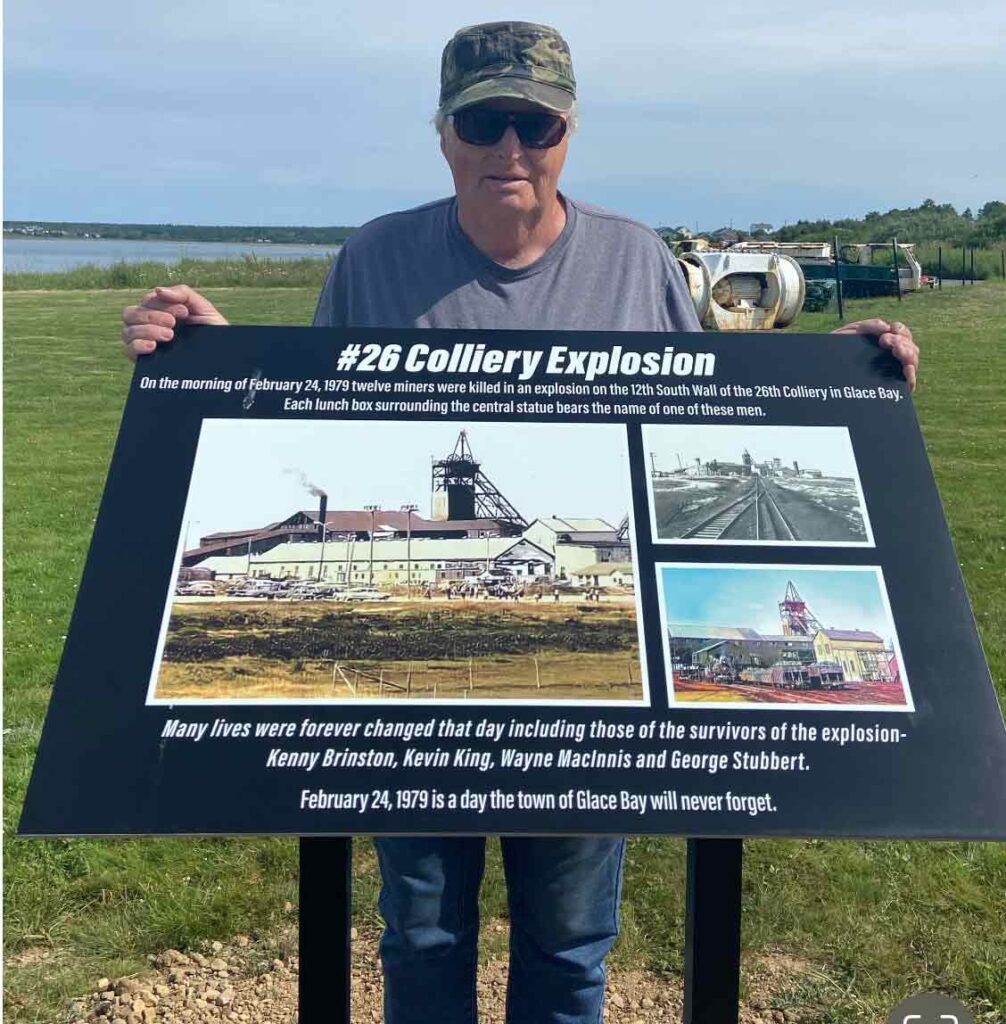 Man stands behind a placard at the site of the mine explosion memorial