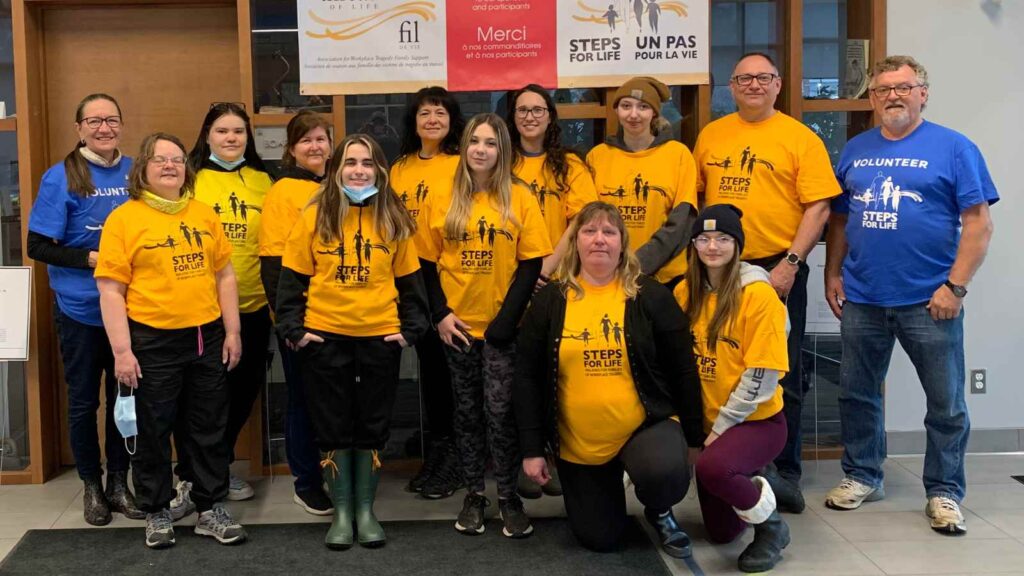 A group of volunteers and walkers in yellow T-shirts stand in front of a Steps for Life thank you sign