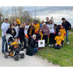 A large family gathers beside a small white sign beside a park path