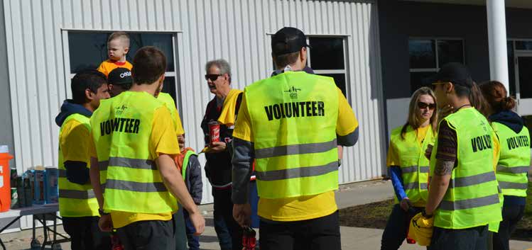 A group of people stand in yellow t-shirts and reflective vests that read "volunteer" across the back.