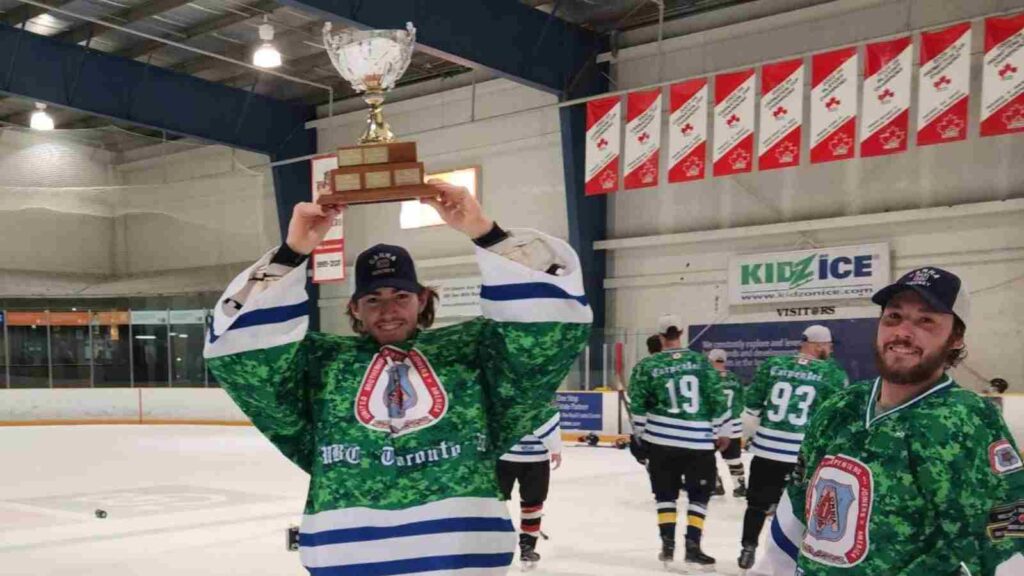 A hockey player holds a championship cup above his head in celebration as another player smiles for the camera. 
