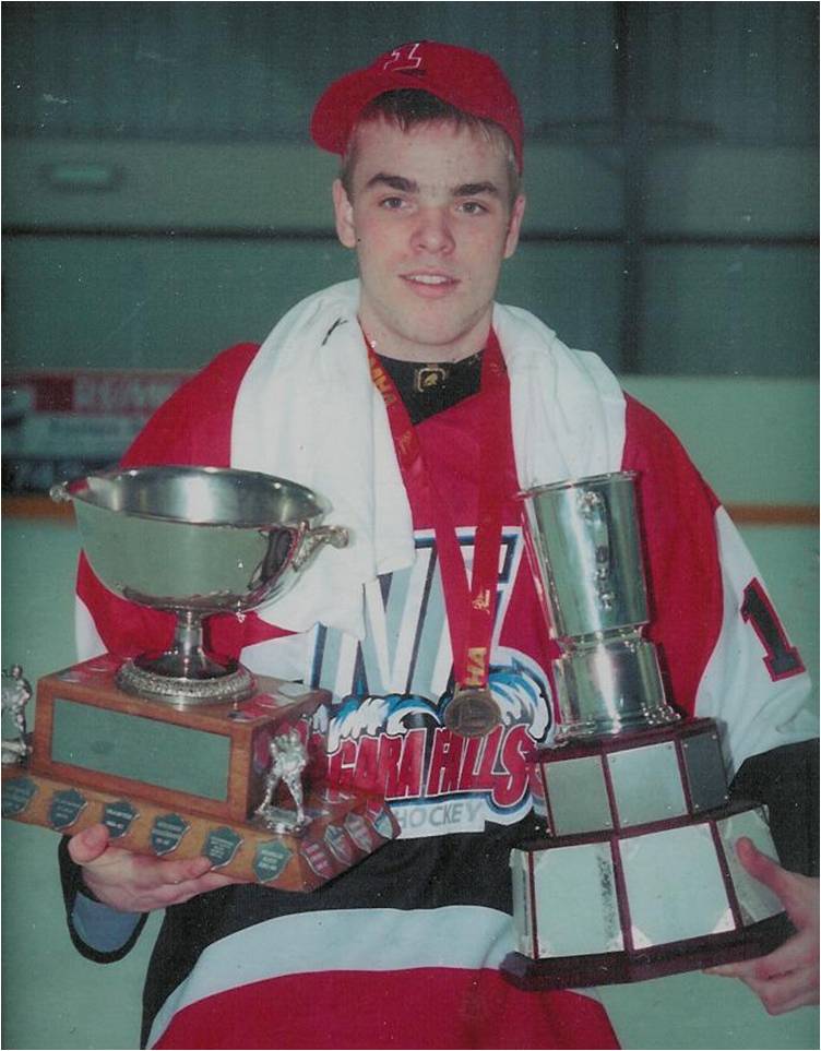 Teenage boy in hockey gear on a rink, holding two silver cups.