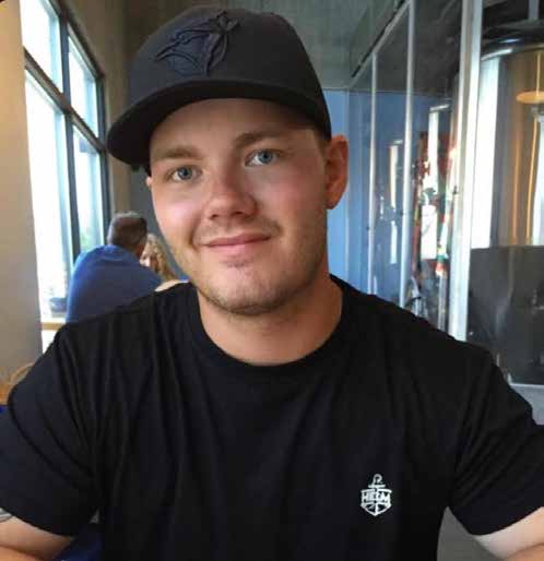 Young man in black T-shirt and black Blue Jays cap sitting at a table in a brewery.
