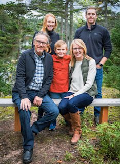 A man, woman and three  children pose for a photo on a bench in the forest. 