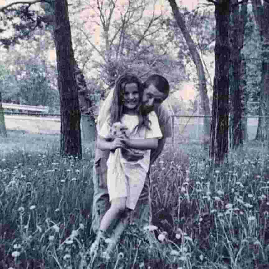 A young girl and her dad in a meadow, in front of some trees.