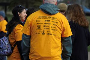 Man wearing yellow t-shirt, seen from the back, displaying various company logos.