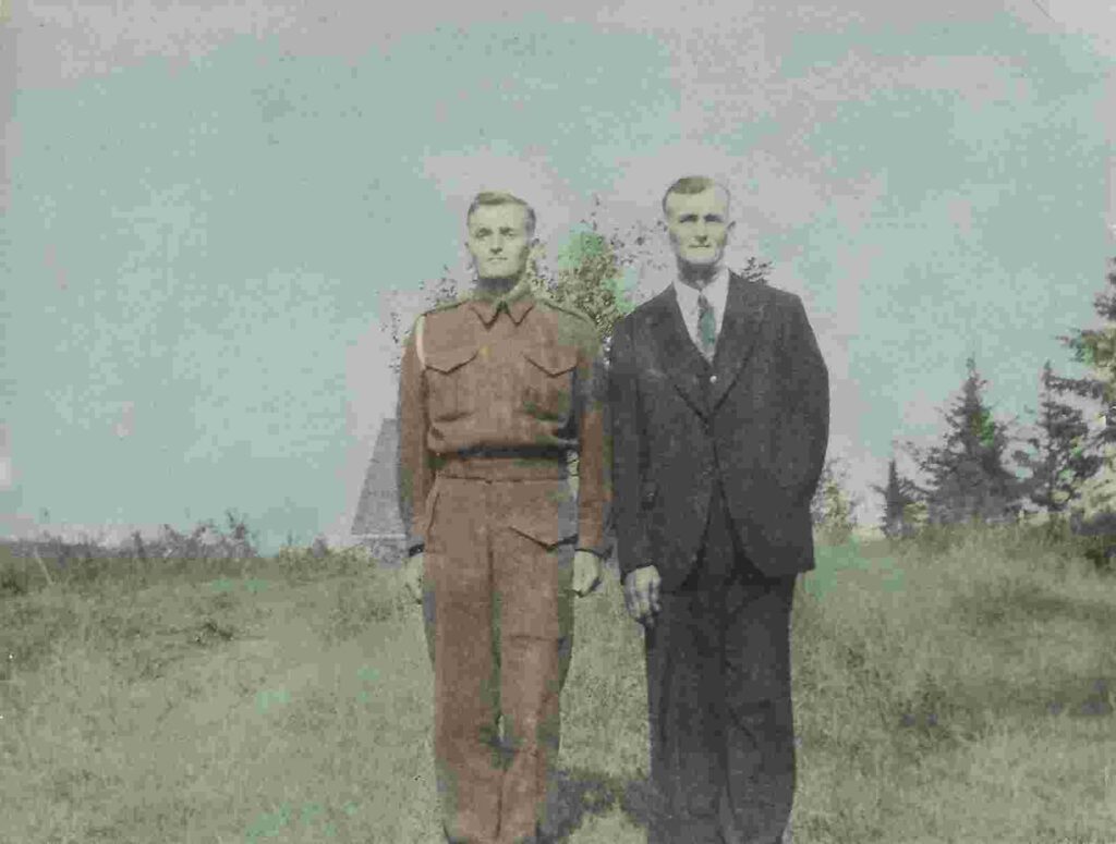 A young man in uniform stands beside an older man wearing a black suit. They look to be in a farmer's field. 