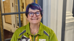 A woman with a large smile, green shirt and purple hair holds a glass star up for the camera.